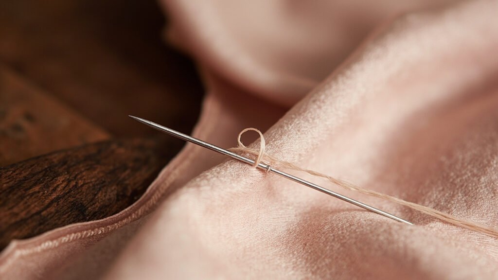 Aiguille fine sur satin rose, fil tiré à réparer.