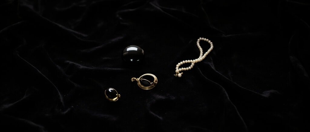 Broche en jais noir, médaillon doré, pendentif onyx et perles sur velours.