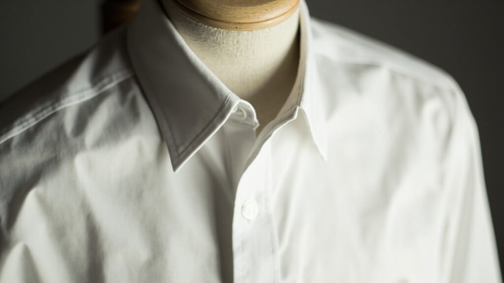 Chemise blanche en popeline sur mannequin de bois, plis nets.