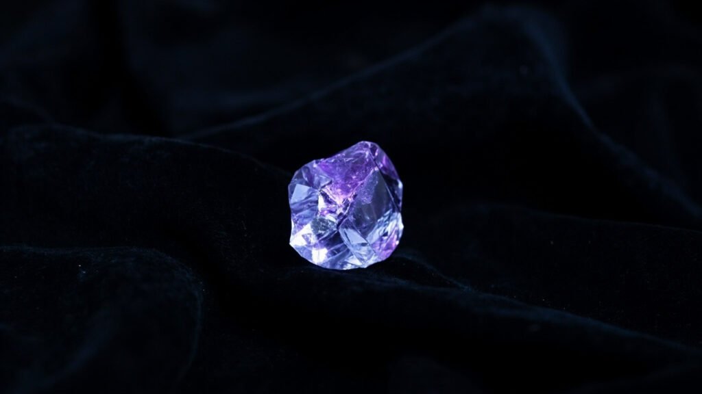 Diamant brut émettant une lueur bleu-violet sur velours noir.