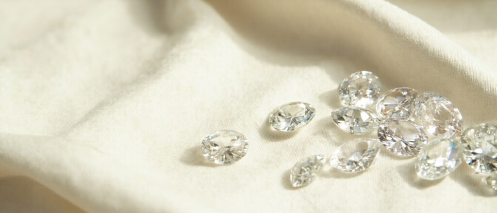 Diversité de diamants taillés posés sur soie crème, formes et tailles variées.