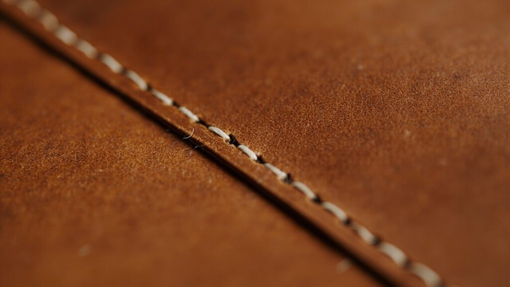 Gros plan d'une couture au point sellier sur cuir cognac