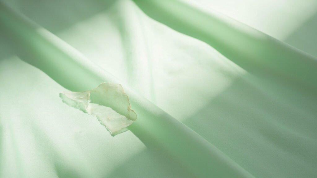 Panneau de soie jade sous lumière rase révélant faiblesses cachées.