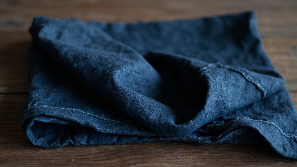 Pli sculptural de lin indigo drapé sur noyer foncé.