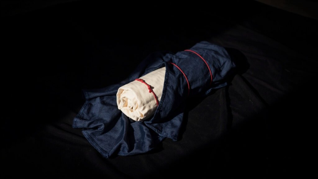 Rouleau de soie brute dissimulé sous tissu indigo, lié d'un cordon rouge.