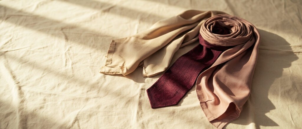 Soie étalée : foulard poudré, cravate bordeaux, carré champagne plié.