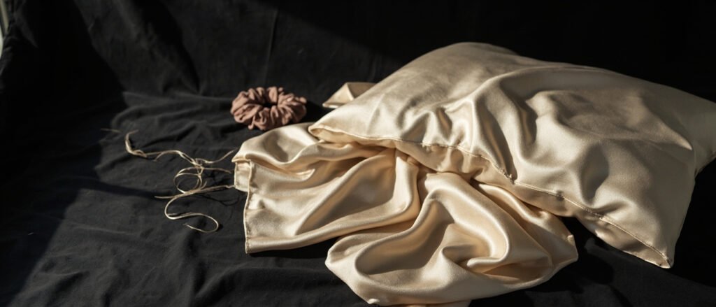Taie et chouchou en satin champagne drapés sur velours sombre.