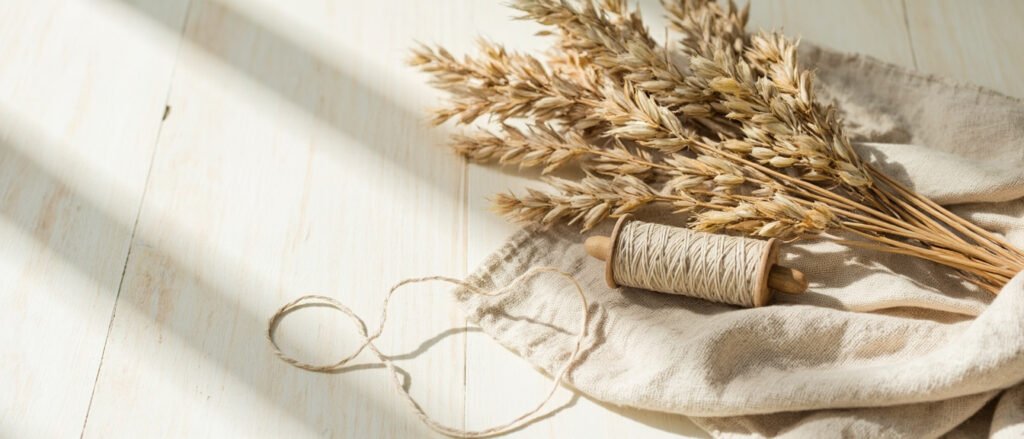Tiges de lin, fil écru et tissu plié sur bois patiné.