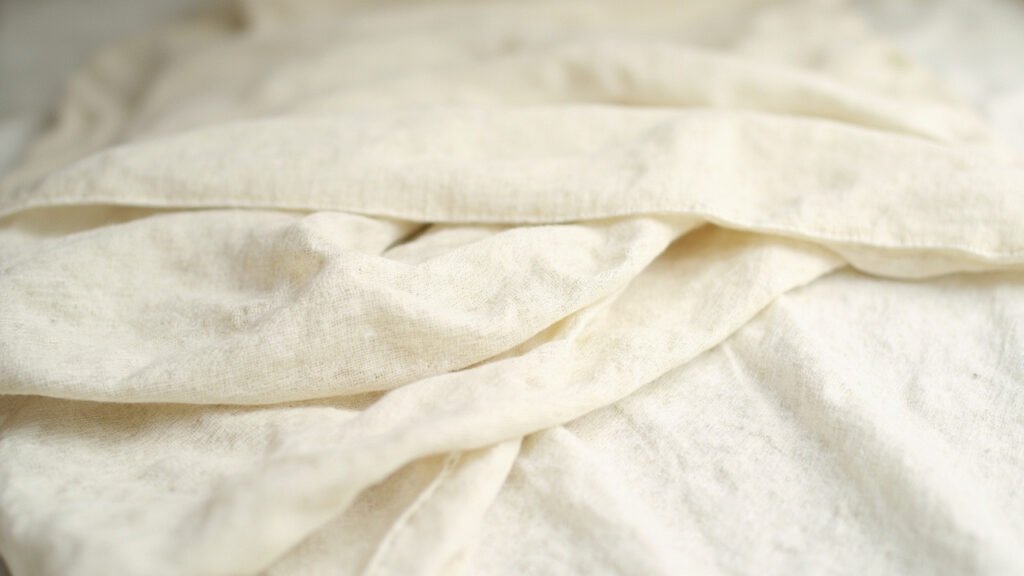 Tissu de lin écru plié révélant texture et tissage authentiques.