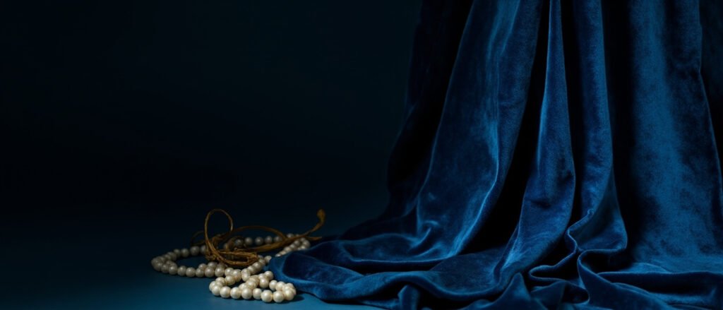 Velours de soie bleu nuit drapé, perles crème, fil d'or, lumière rasante.