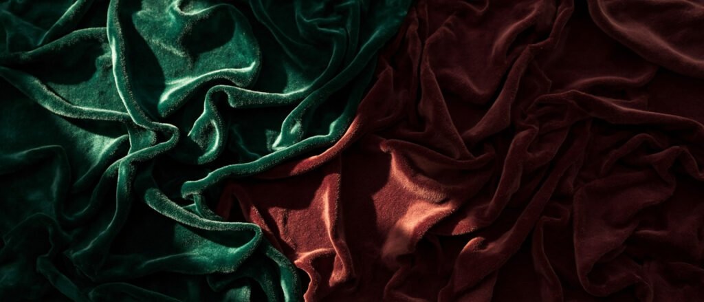 Velours émeraude et bordeaux drapé en plis somptueux, lumière chaude.