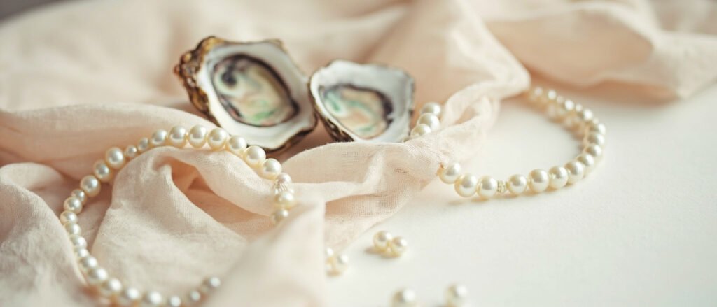 Bracelet de perles sur lin écru près de coquilles d'huîtres ouvertes.