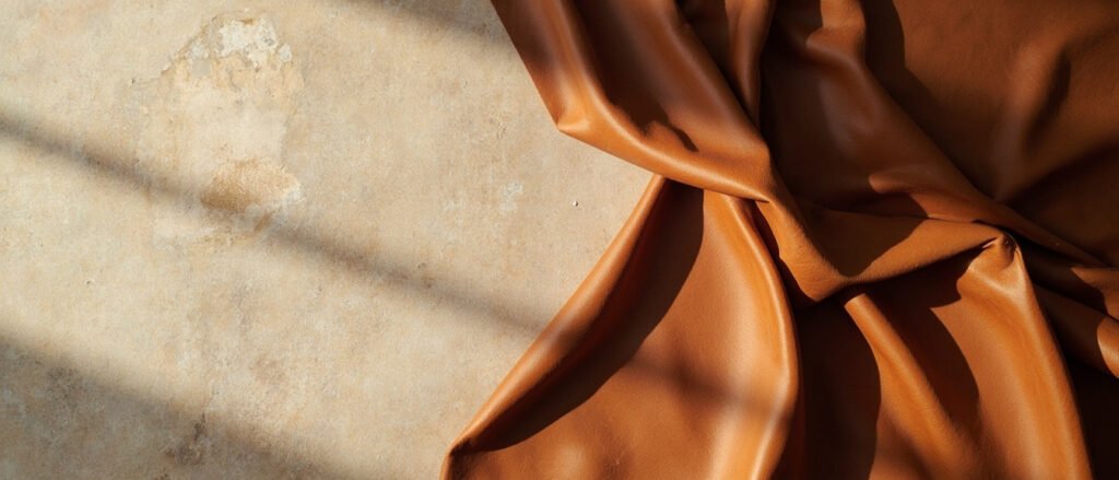 Cuir pigmenté cognac drapé en plis, patine d'occasion subtile, espace vide à gauche.