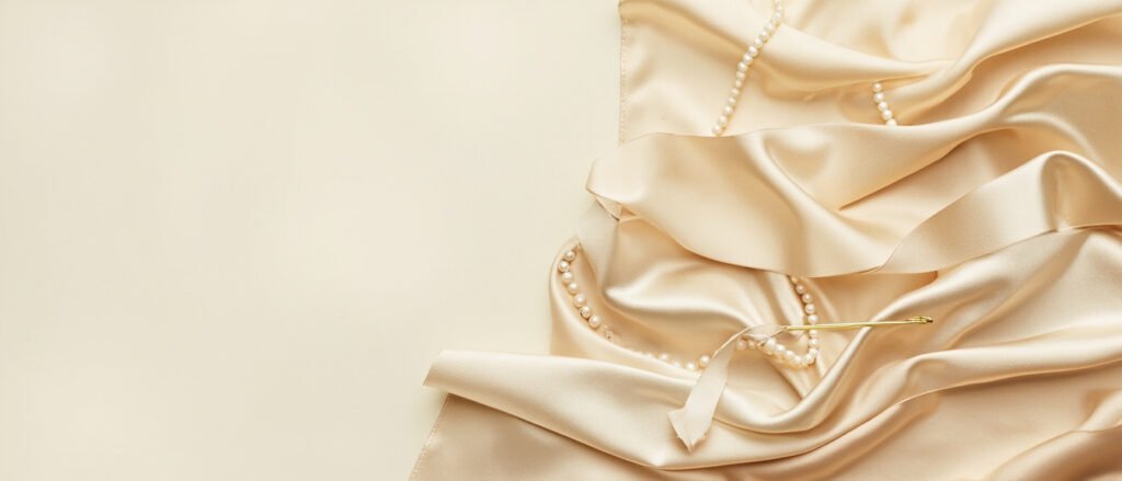 Drapé de satin champagne et perles sur fond clair, lumière douce.
